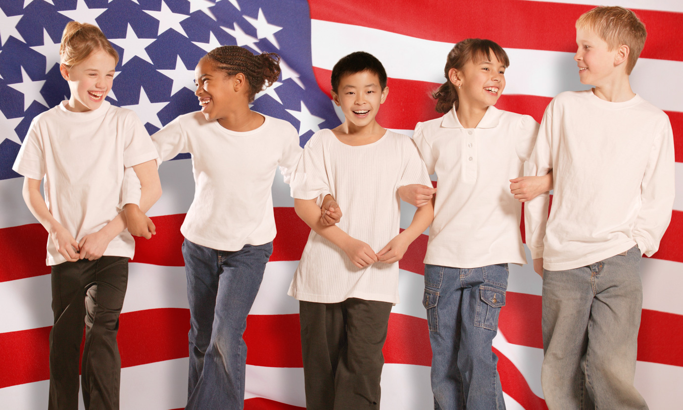 Smiling children standing arm-in-arm in front of American flag.