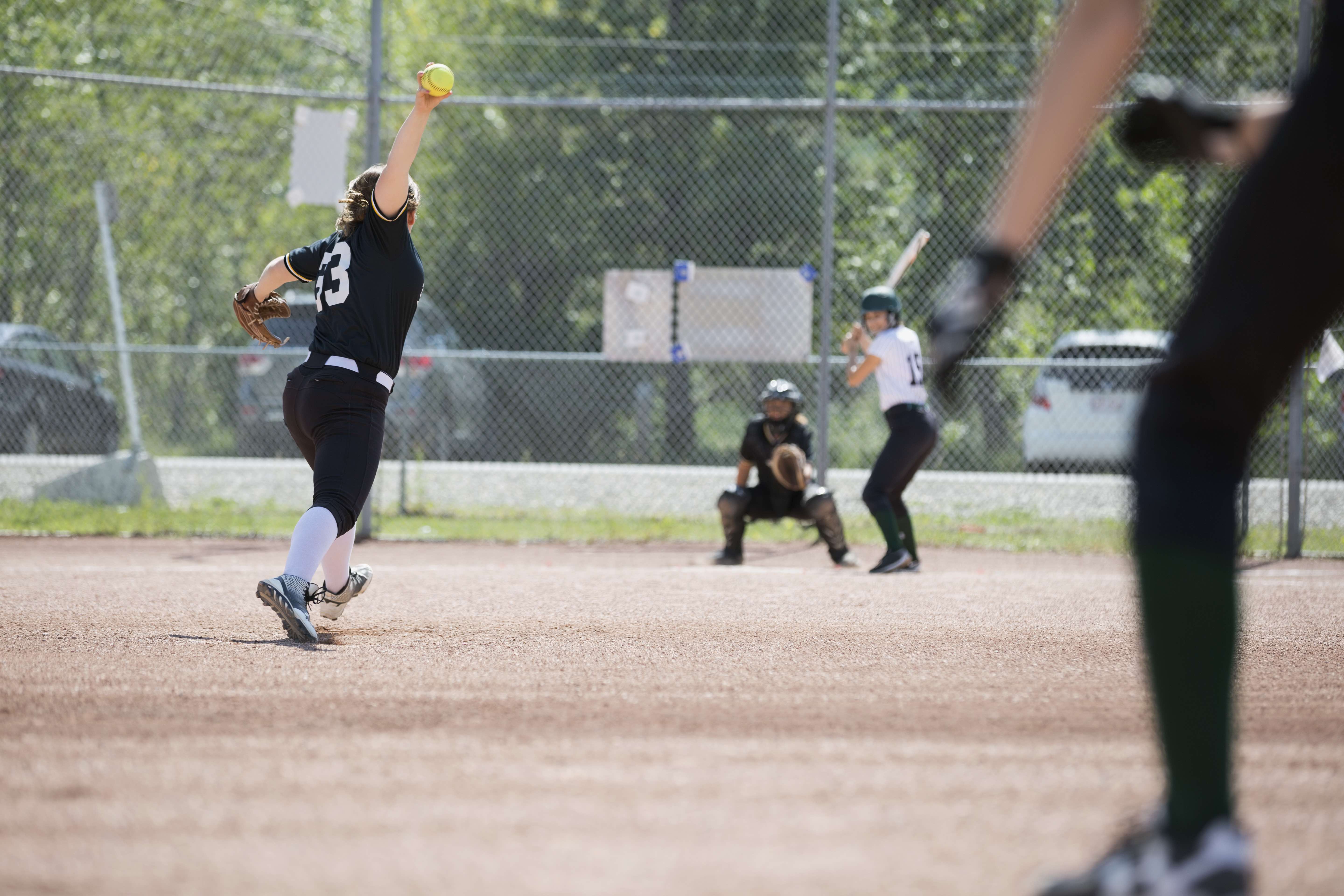A softball player pitches the ball to the batter.