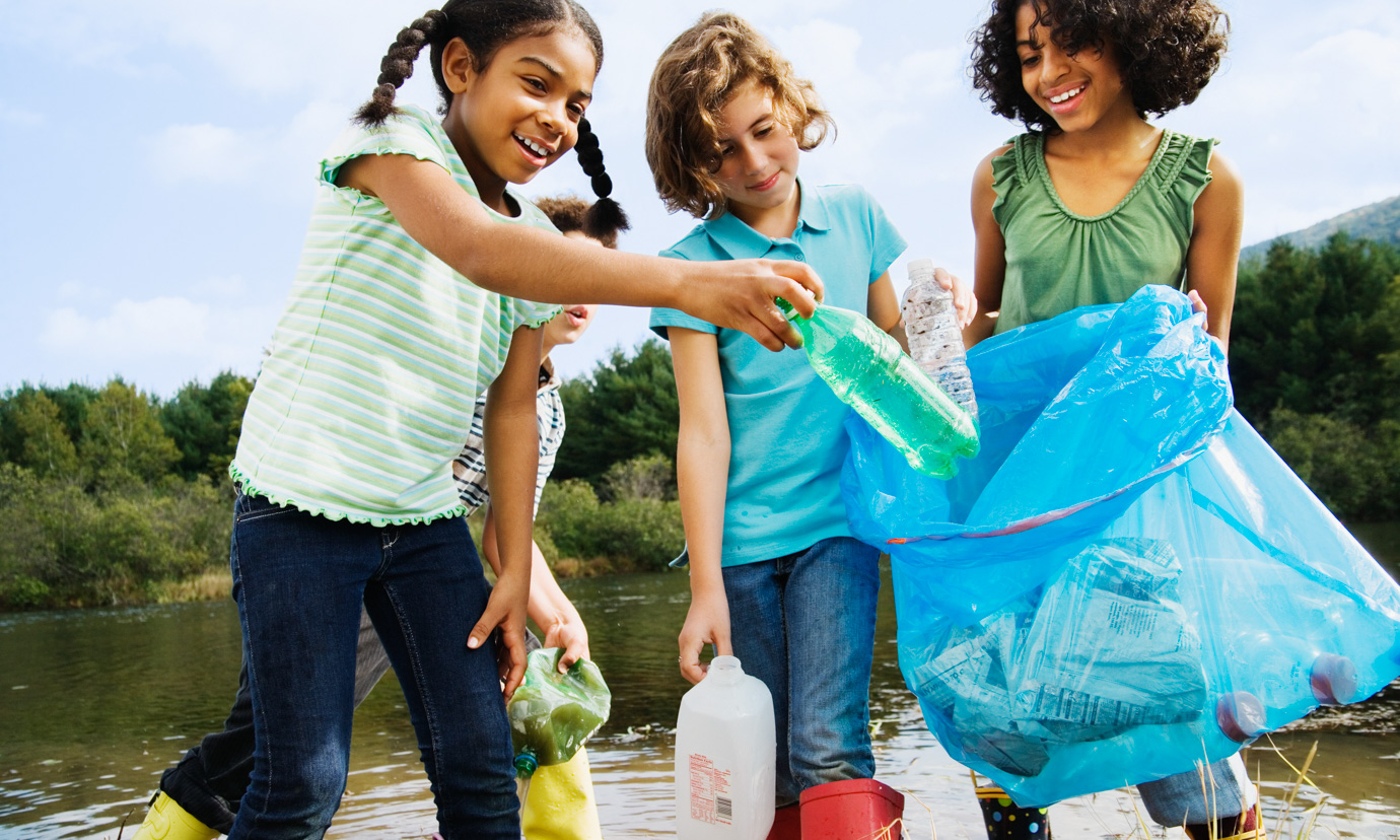 Three girls picking up plastic bottle litter from a pond.