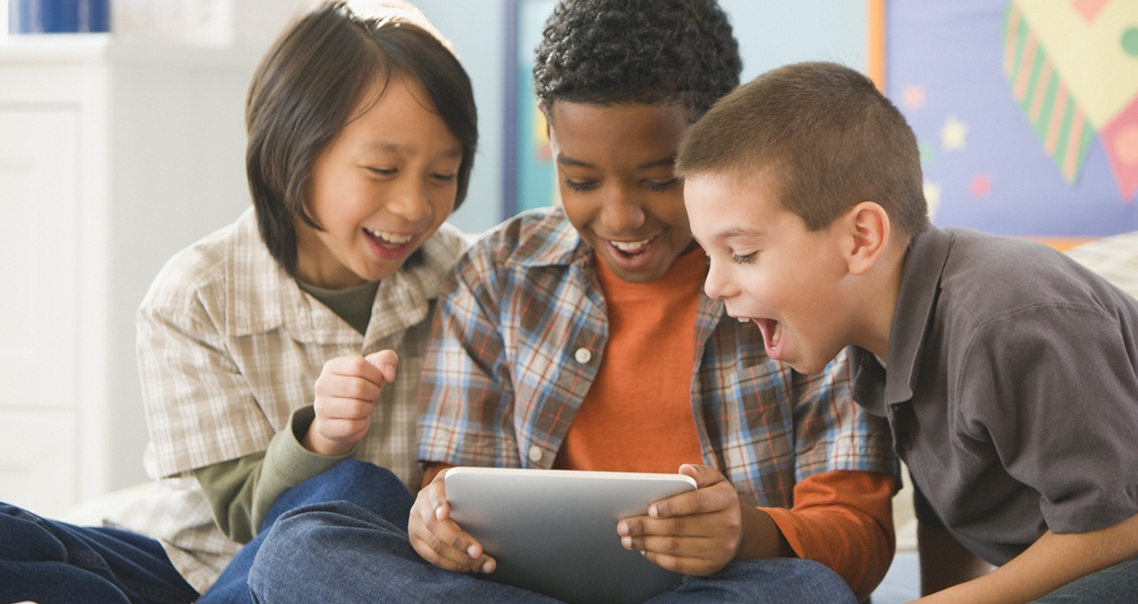 Three boys looking at a digital tablet and laughing together.