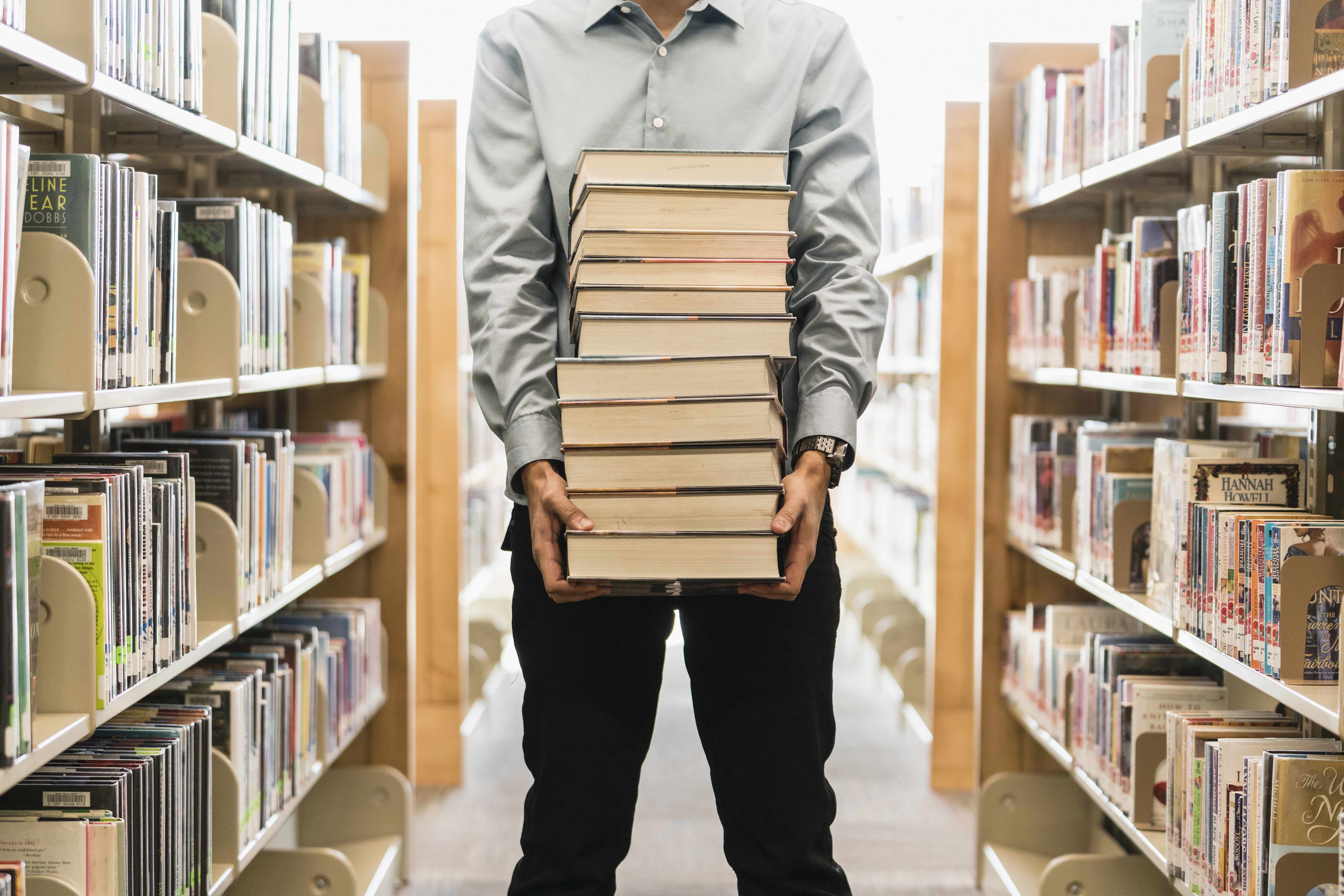 A man carries a stack of books in a library.