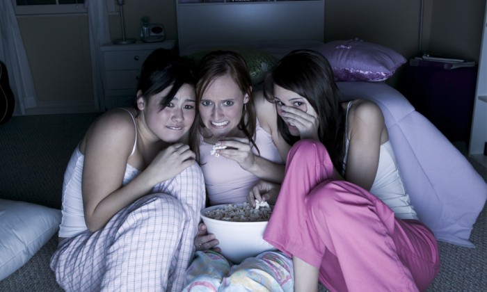 Three girls watching a scary show and eating popcorn