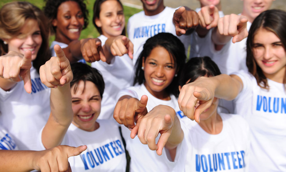 Happy and diverse volunteer group pointing towards camera