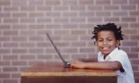 Boy (8-10) at desk with laptop, smiling, portrait
