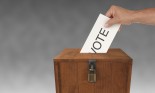 A man's hand putting an envelope in a ballot box
