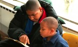 Mentor and child reading book age 14 and 6 at the community youth center