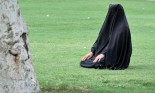 Woman sitting on grass in full hijab, wearing paranja