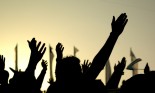 A crowd of people in silhouette raising their hands against the background of a yellow sunset