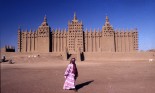 Woman walks past the Mosque in Djenne, Mali