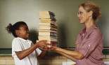 Girl (10-12 years old) handing a pile of books to woman in classroom
