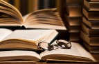 Opened book, lying on the bookshelf with a pair of glasses