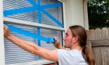 Young man taping windows on his home in preparation for a hurricane