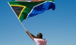 African man waving a South African flag against blue sky