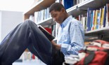 African-American teenager reading book in library