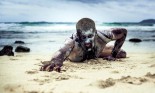 Young man with zombie body painting, covered with mud on the beach