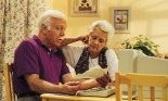 Elderly couple sitting at kitchen table working on a computer.