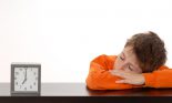 boy asleep on desk beside clock