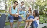 Teenage friends (13-17 years old) hanging out, using smart devices outdoors