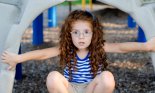 Red headed little girl looking scared looking through a playground