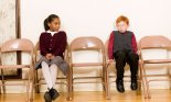 Girl and boy sitting in chairs against wall
