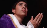 A teenage boy wearing a purple robe performs in a theatrical production.