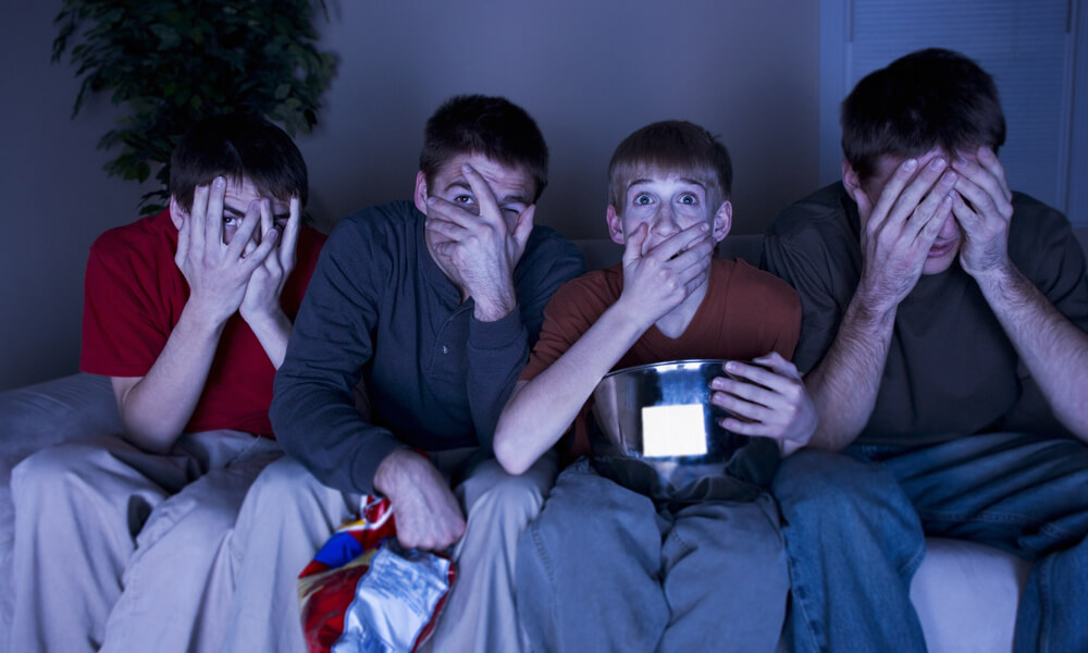 Four boys watching a scary show and eating popcorn