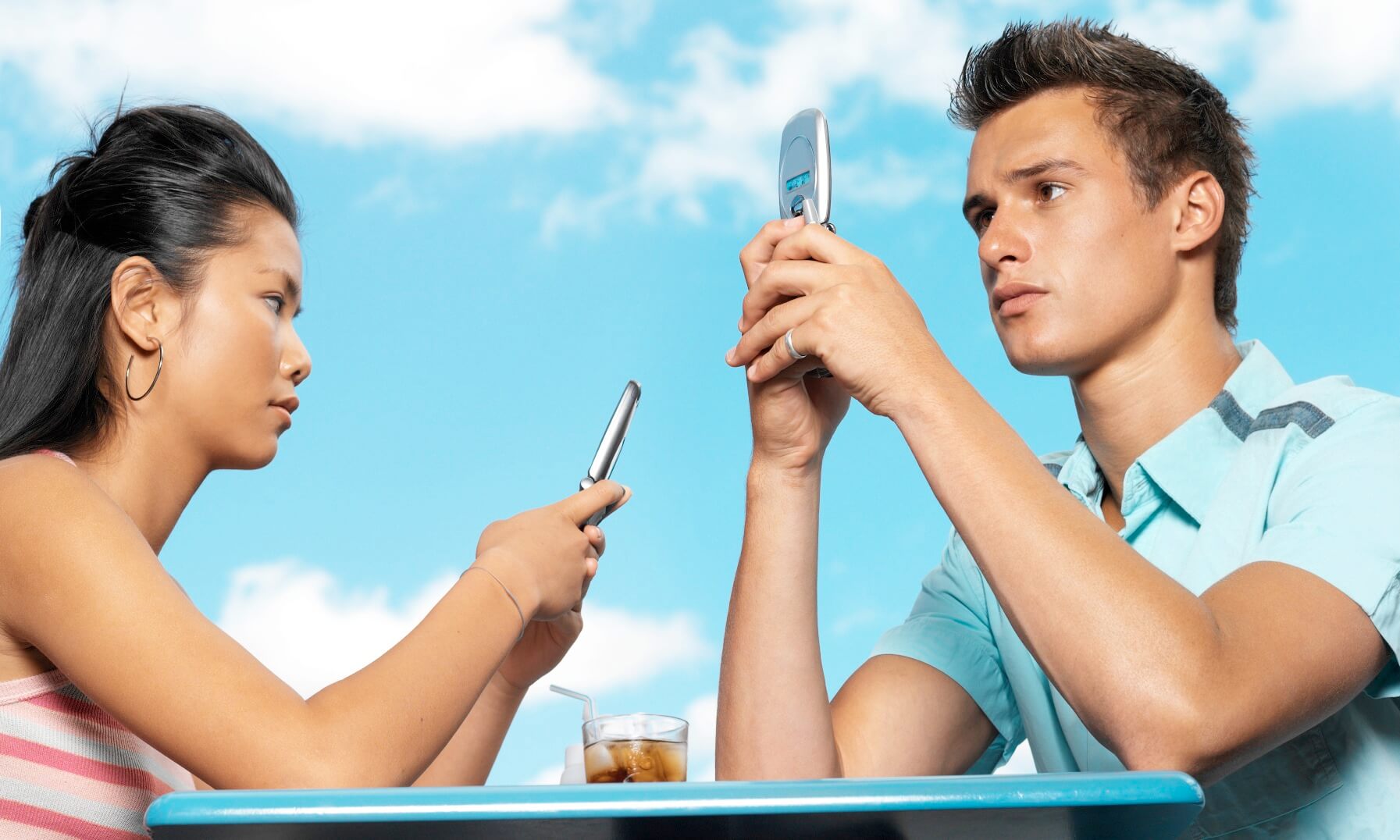 Teenage couple preoccupied with their cell phones ignoring each other at a cafe table