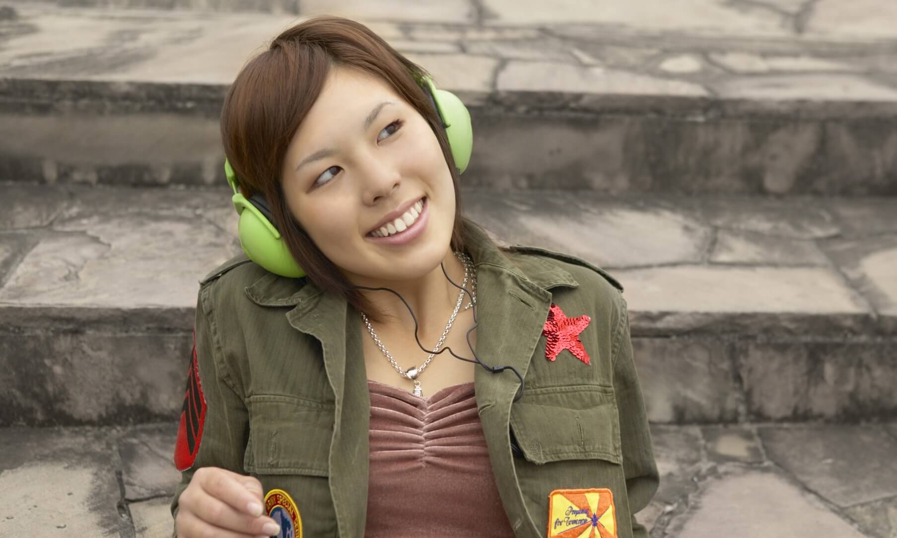 Teenage girl sitting outside on steps listening to headphones