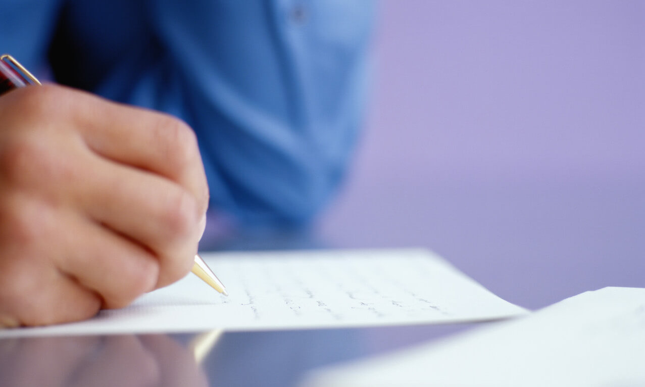 Close up of person's hand as they write on a piece of paper.