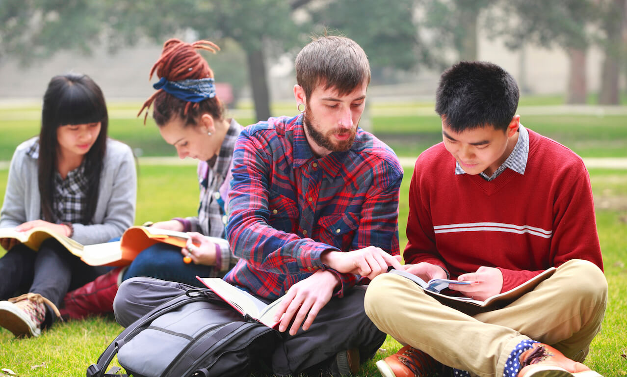 Two Chinese students and two Caucasian students sitting on the grass, studying together