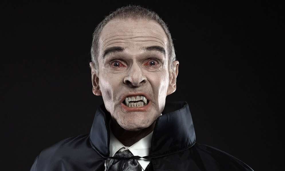 Studio shot of Dracula with black cape showing his fangs, against black background