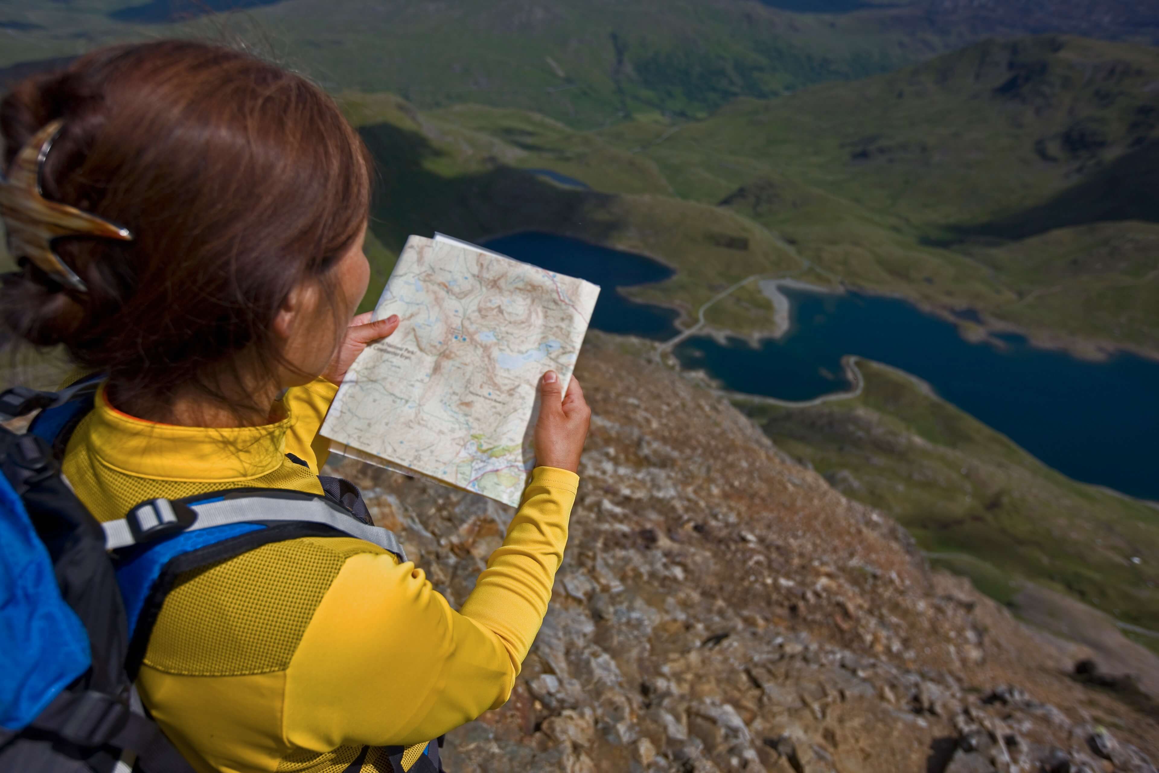 Over-the-shoulder shot of hiker reading map on mountainside.