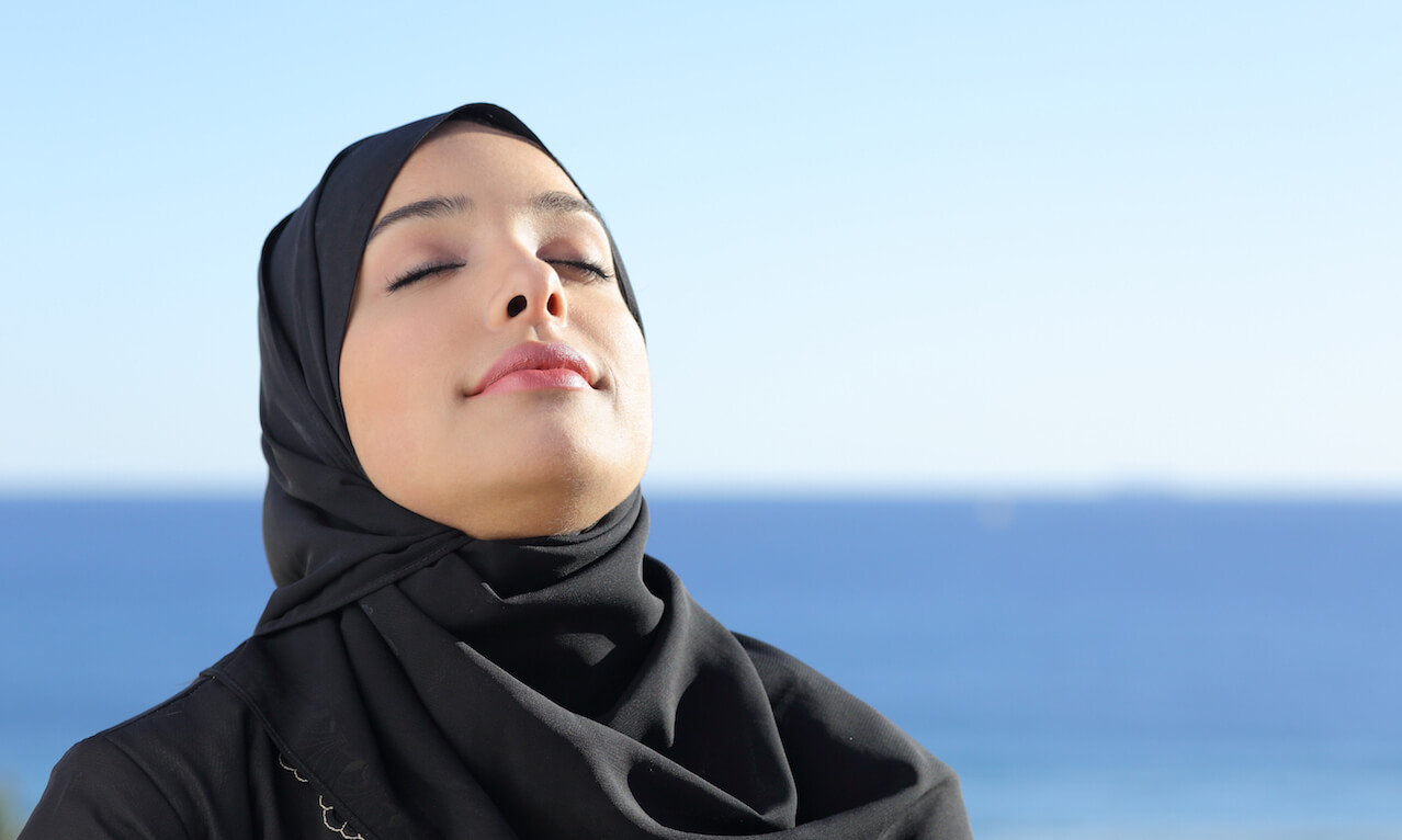 Arab Saudi woman breathing deep fresh air in the beach with the ocean and horizon in the background