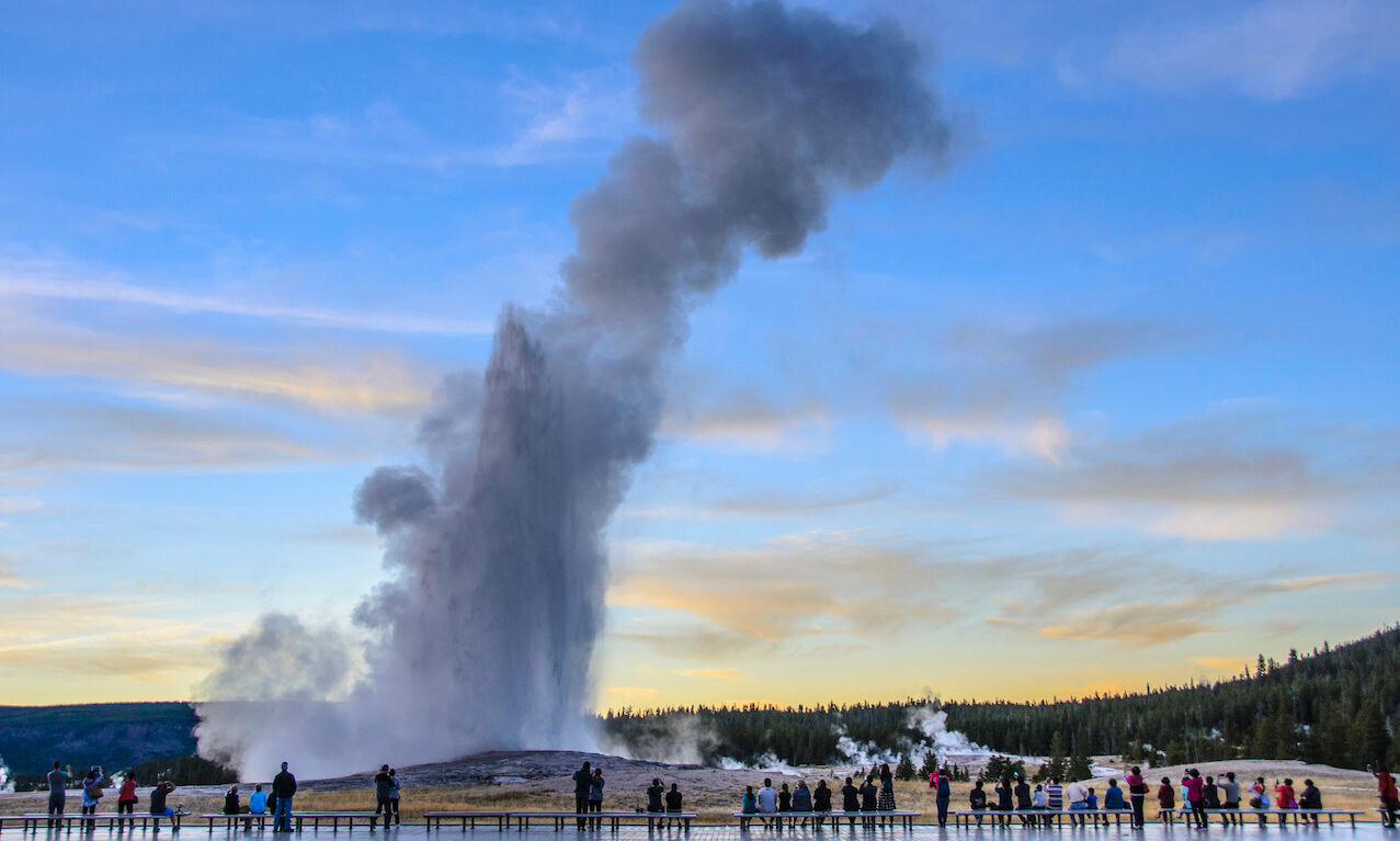 Groups of people have been waiting to watch, experience and photograph this Old Faithful eruption just after sunset on a sunny early autumn day.