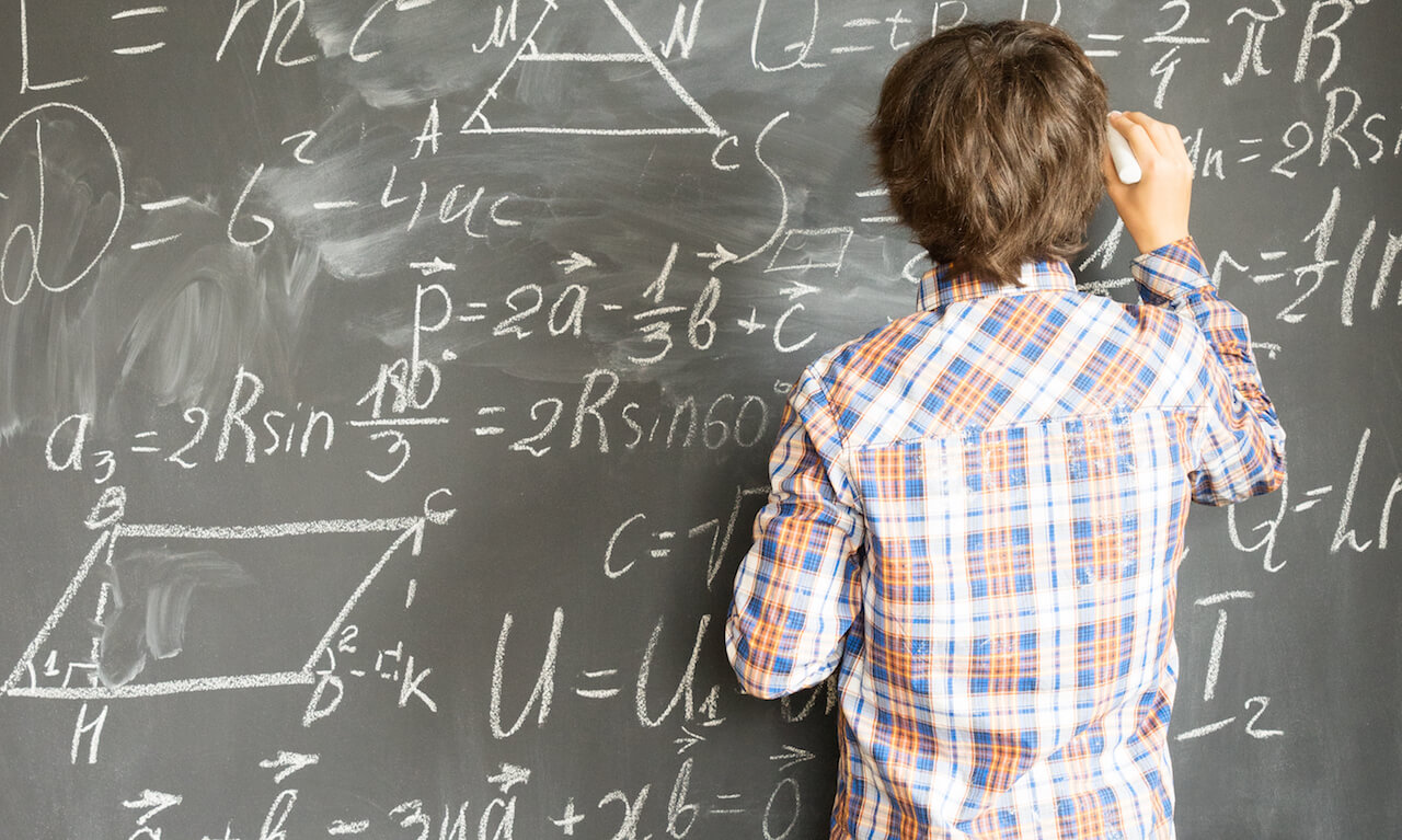 Boy with chalk writing complicated math formulas on black board