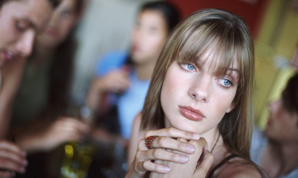 Teenage girl looking bored and lonely while sitting at a table with a group of friends Teenage girl looking bored and lonely while sitting at a table with a group of friends