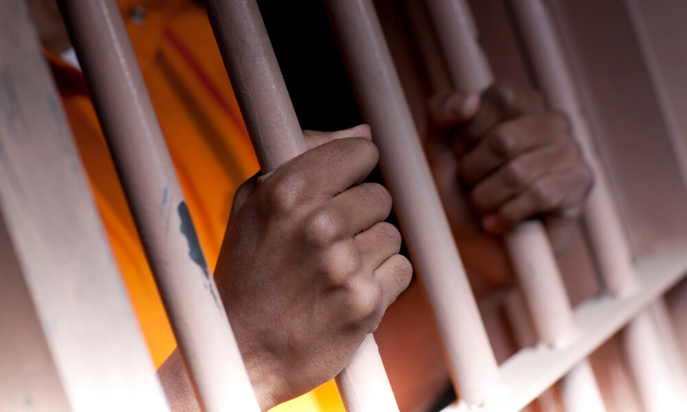 Close-up of hands gripping the bars of a prison cell