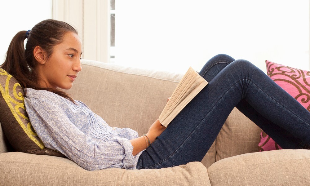 Teenage girl (14-15 years old) reading on sofa