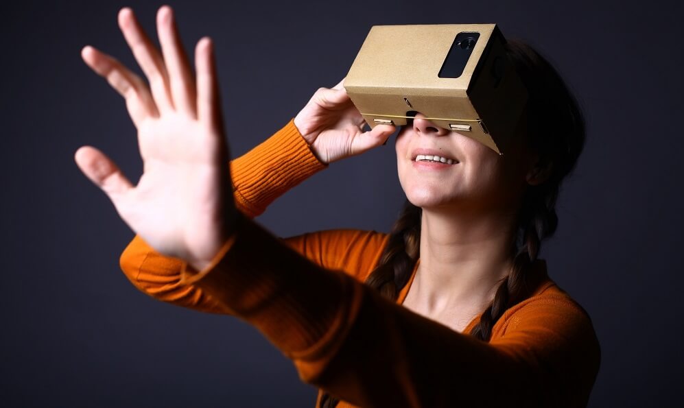 Girl looking through a cardboard device with which one can experience virtual reality on a mobile phone