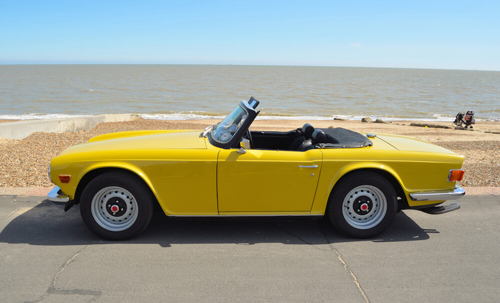 vintage yellow car parked in front of a beach
