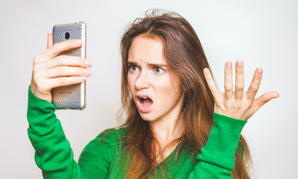 Young woman with an expression of shock or disgust looking at a smartphone in her hand