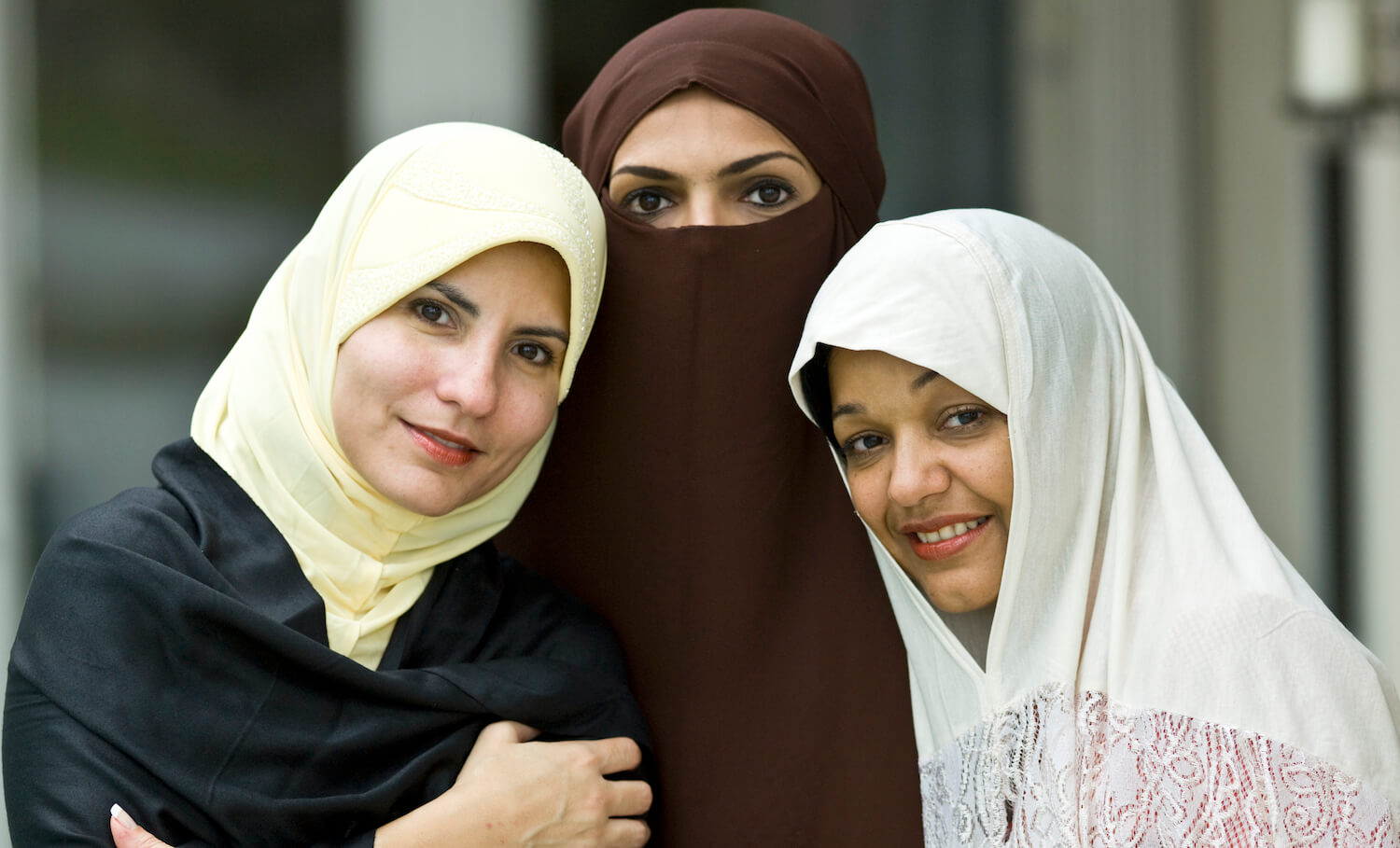 two women wearing hijabs smile next to one woman wearing a burqa