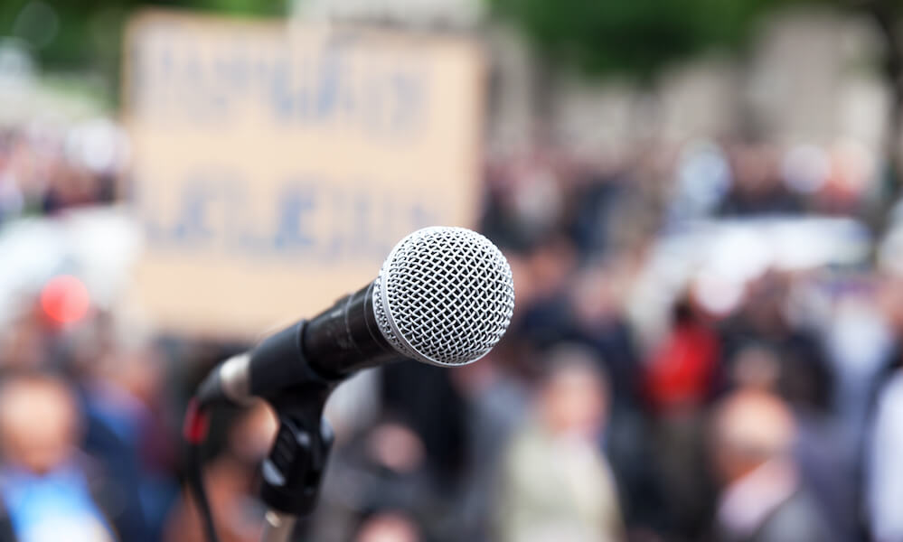 Protest. Public demonstration. Microphone in focus against blurred crowd.