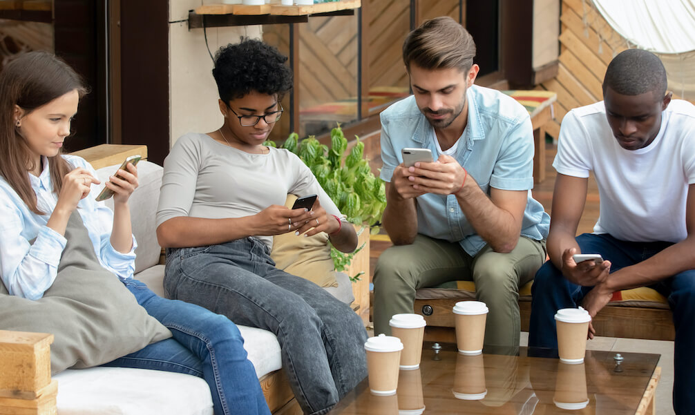 Diverse young friends sitting together using phones