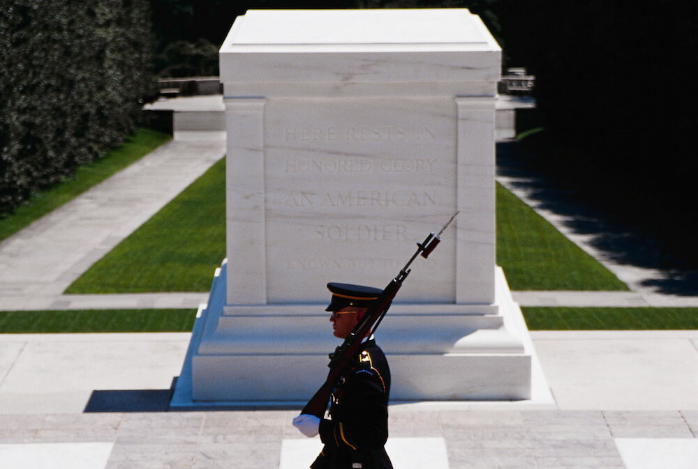 a soldier wielding a rifle stands guard in front of the Tomb of the Unknowns in Arlington National Cemetery