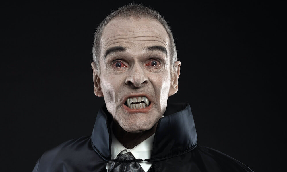 A close-up of Dracula: he is wearing a cape and has red eyes and sharp fangs.