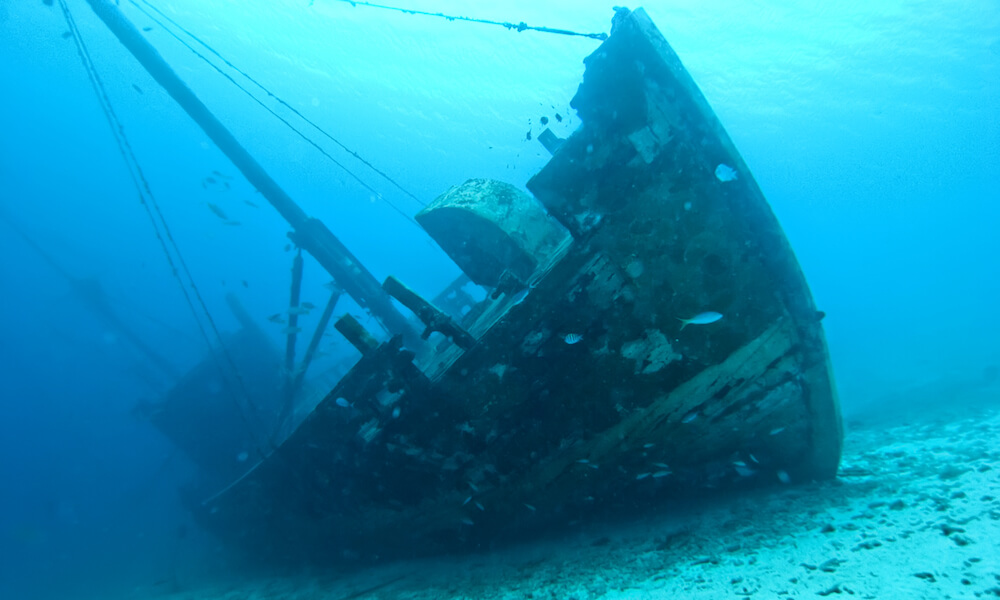 A large wooden ship sits canted on the sea floor. It is slightly weathered but still intact and well-preserved.