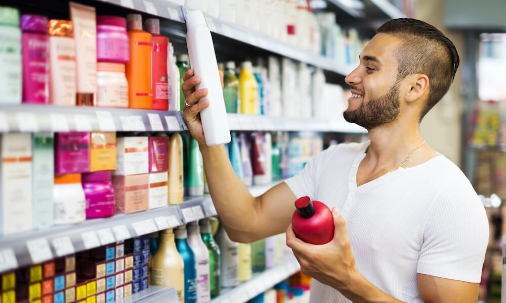 Smiling man chooses shampoo in supermarket