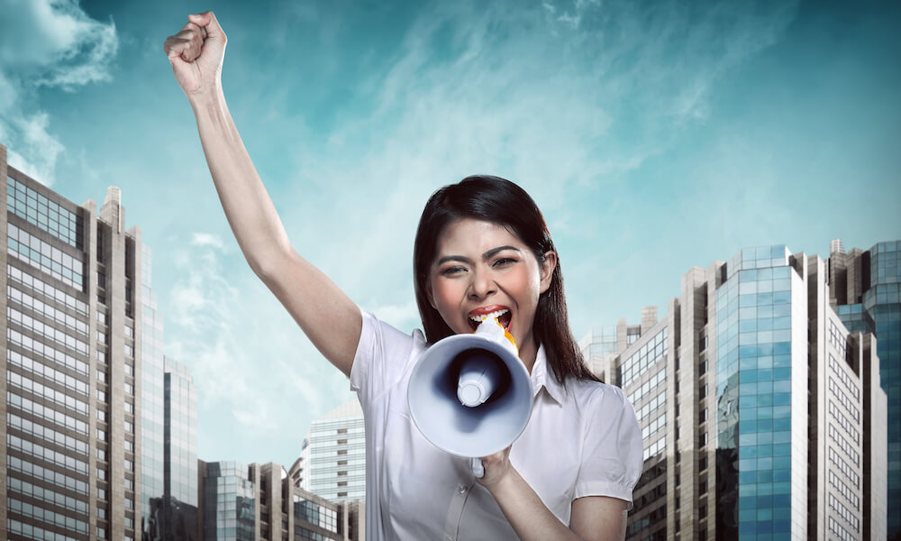 Asian woman shouting into a megaphone, raising her fist