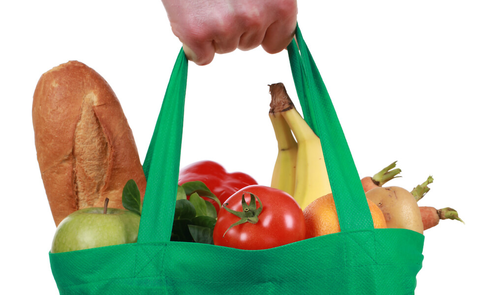 Hand holding a bag filled with groceries, isolated on white